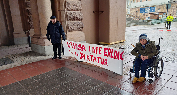 Två personer är utanför riksdagens hus. En av dem sitter i rullstol. De håller i ett plakat där det står Utvisa inte Erlin till en diktatur.