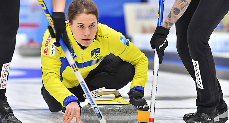 Från en match i curling. Anna Hasselborg skickar iväg en sten. Två andra sopar framför stenen.