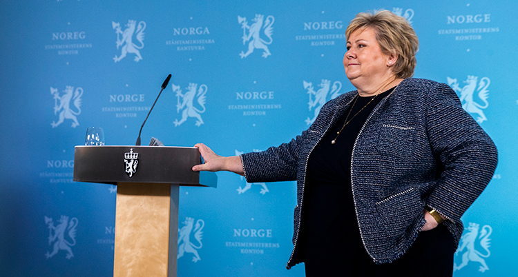 Solberg ser bister ut. Hon står vid en talarstol och håller handen på den.