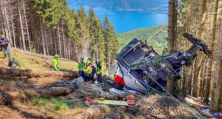 En vagn från en linbana ligger på marken. Den är trasig. Räddningspersonal står vid vagnen.