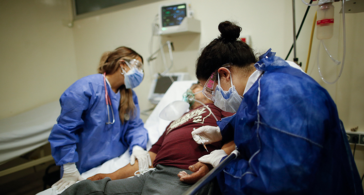 En patient ligger i en sjukhussäng. Vårdpersonal med masker står bredvid.
