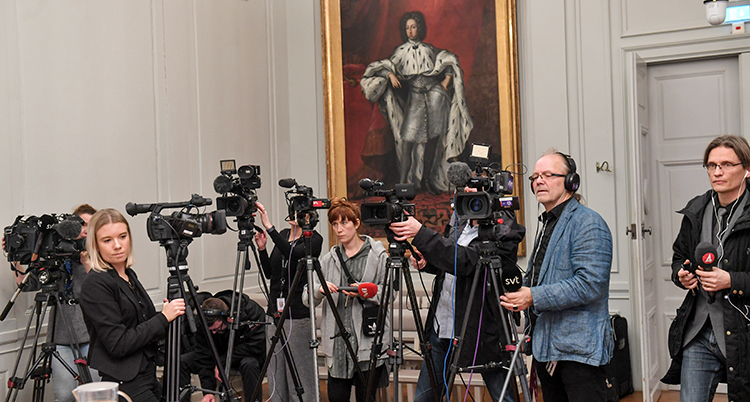 journalister trängs med flera mikrofoner och tv-kameror i ett rum.