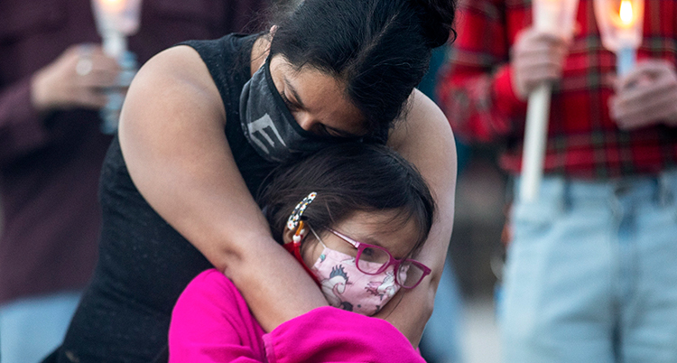 En kvinna kramar om ett barn. De är ledsna. Båda har munskydd.