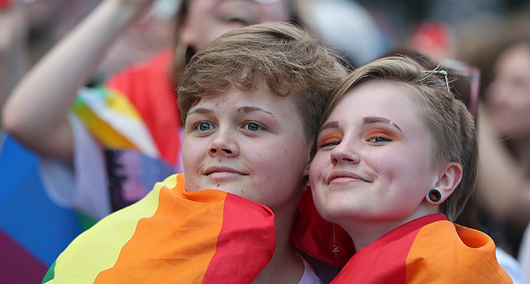 En nära bild på två ansikten. De är insvepta i regnbågsflaggan.