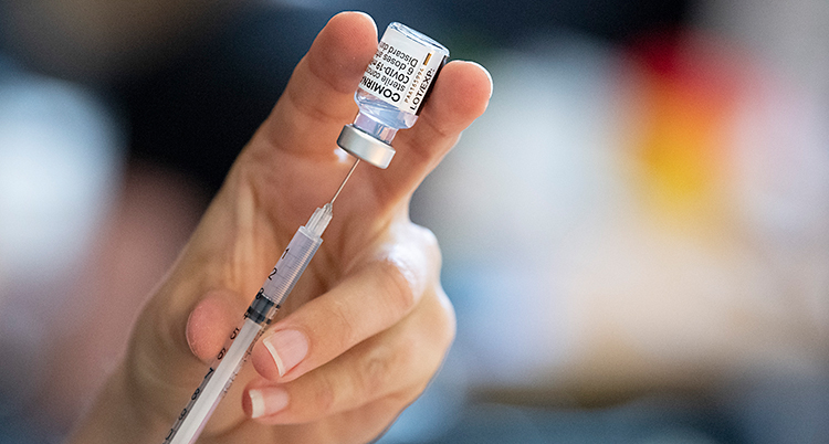 En hand håller i en spruta och en liten burk med vaccin.