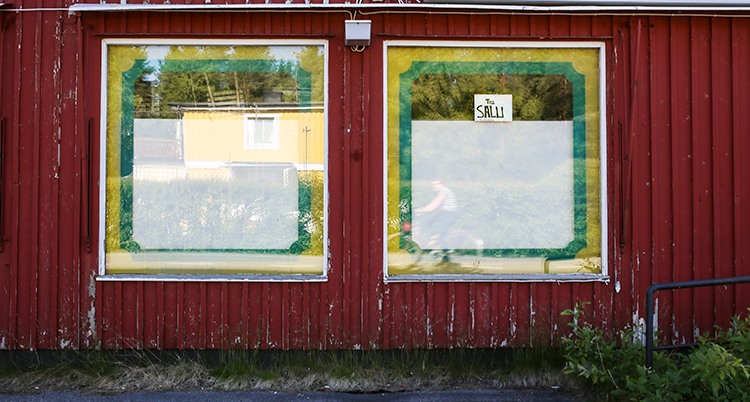 En röd träfasad där två igenbommade skyltfönster syns.