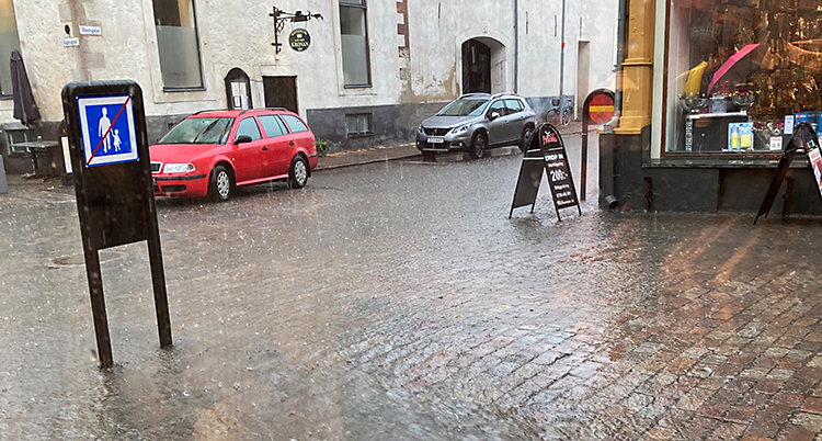 En bild från en gata som är fylld av vatten. Längs vägkanterna i staden står bilar.