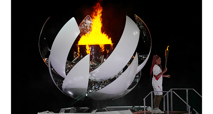 Elden brinner i en vit formation. Till höger står en kvinna i vitt och med en fackla.
