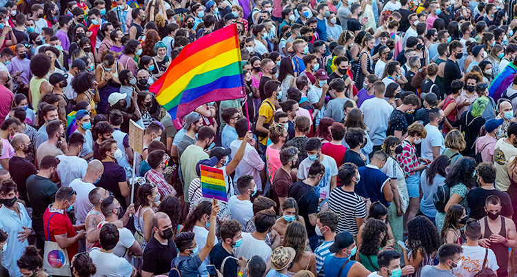 Massor av människor står tätt tillsammans. Flera har Prideflaggor i händerna.