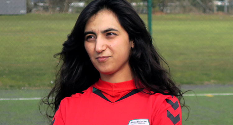 En bild på Khalida Popal. Hon står på en fotbollsplan. Hon har långt mörkt hår och en röd fotbollströja.