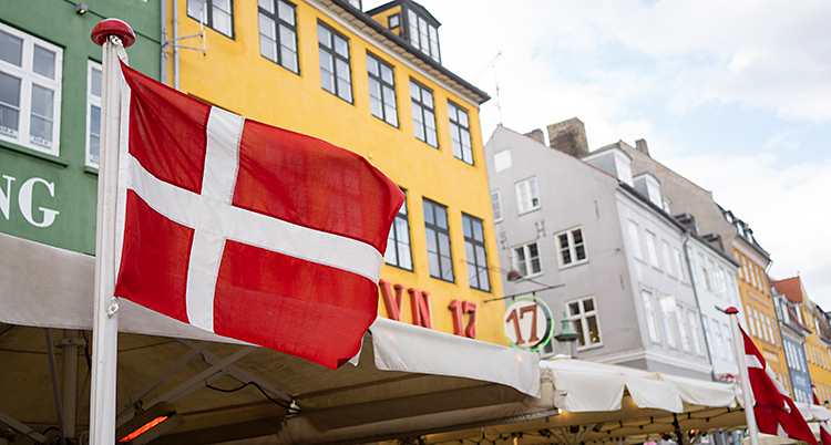Bilden visar hus i området Nyhavn i Köpenhamn. Framför husen finns det uteserveringar och danska flaggor.