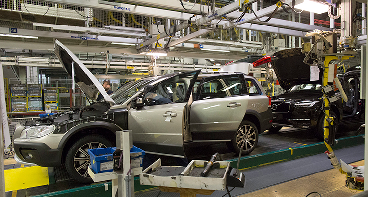 En bil blir tillverkad i en fabrik. Den står på ett band och har motorhuven uppfälld.