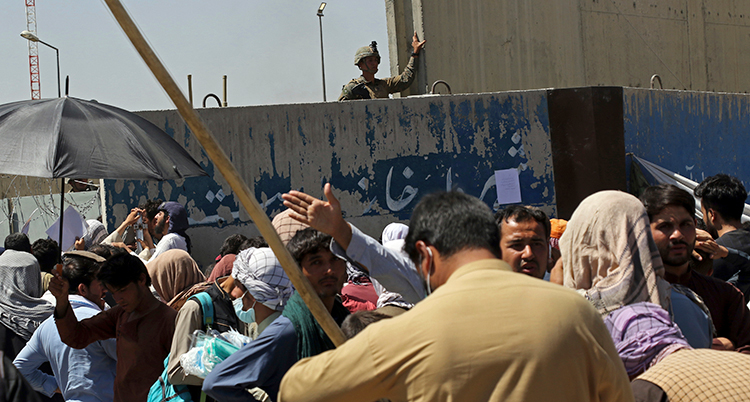 Människor står packat utanför en mur, ovanför muren syns en militär