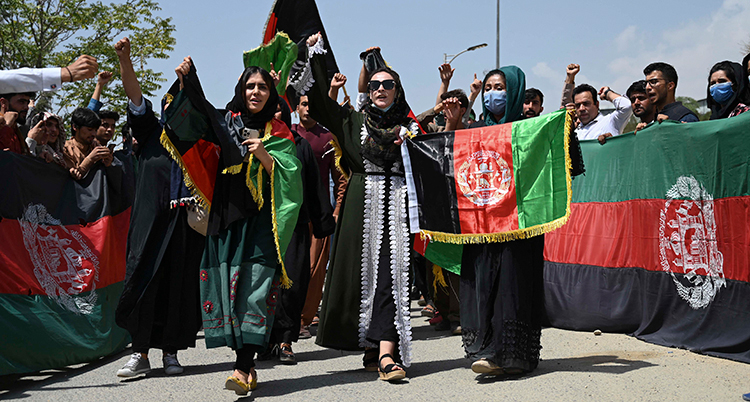 En grupp personer går på en gata. De har knutna nävar i luften och bär en afghansk flagga.