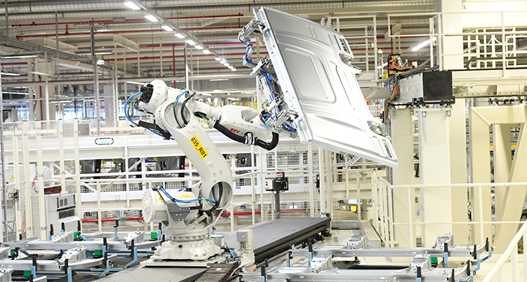 En bild inifrån fabriken där lastbilar blir tillverkade. En robotarm lyfter en lastbilsdel.