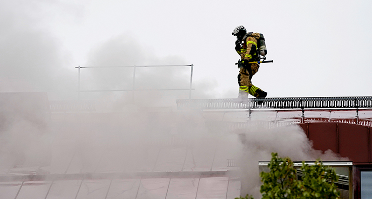 Brandmannen går på taket. Rök väller upp från taket.