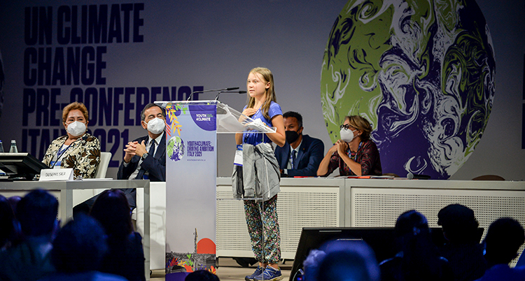 Greta Thunberg står på ett podium vid en talarstol och pratar.