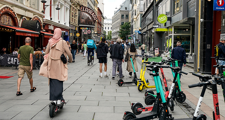 Folk går på gatan. En kvinna åker på en elsparkcykel.