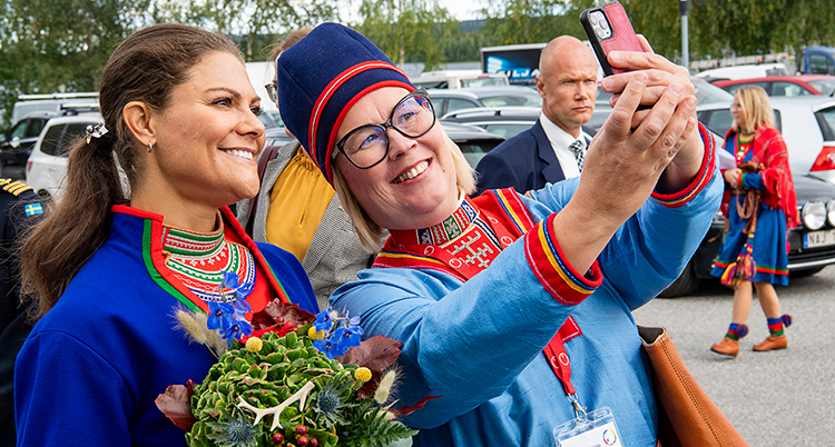 De står bredvid varandra i samiska kläder och kvinnan tar en selfie med mobilen