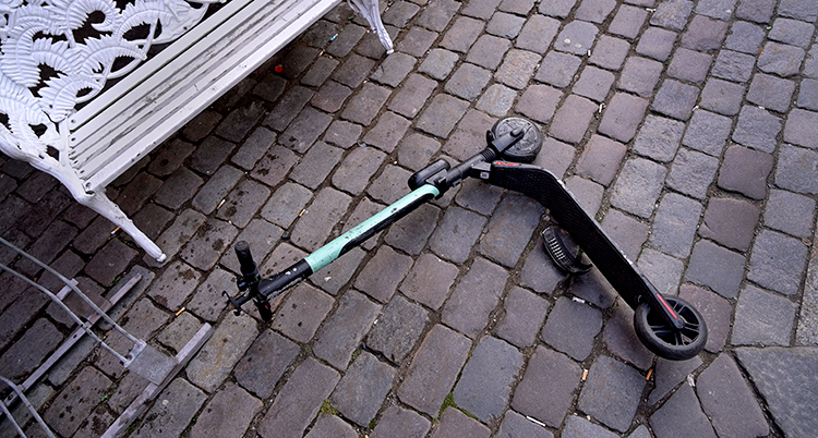 En sparkcykel på el ligger slängd på marken.