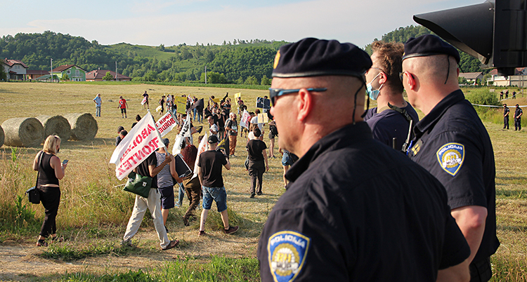 Människor protesterar på ett stort fält. Poliser tittar på.