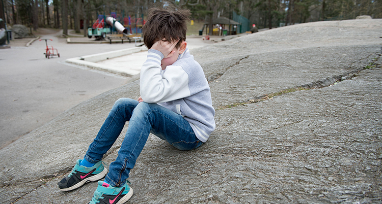 Ett ledset barn sitter i en lekpark. Han har ansiktet i sina händer.