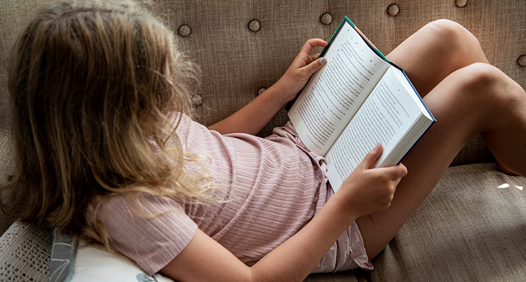 Ett barn sitter i en soffa med en bok i famnen.