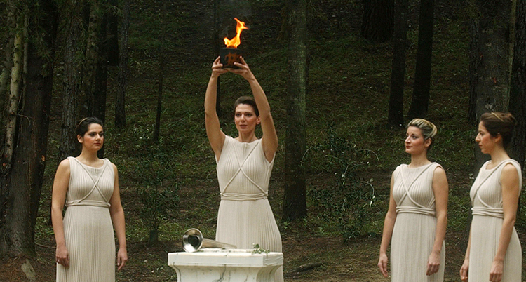 En kvinna i vitt lyfter en eld. Tre andra ser på.
