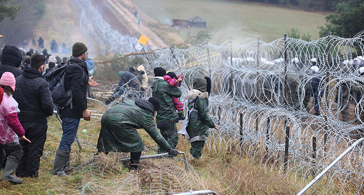 Vuxna och barn är fast framför ett staket i Belarus. De är vid gränsen mot Polen.