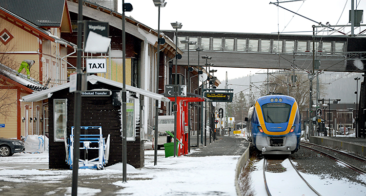 Ett blått och gult tåg står på rälsen vid en station.