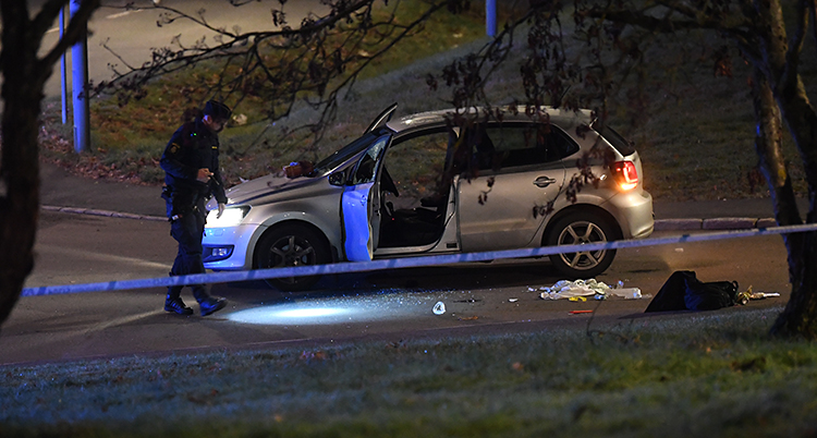 En polis går vid en bil och lyser med en ficklampa.
