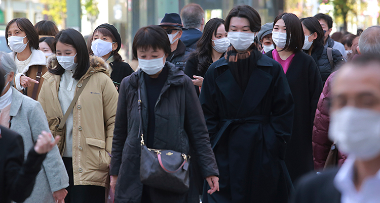 Människor som går på gatan i staden Tokyo i Japan. De har munskydd på sig.