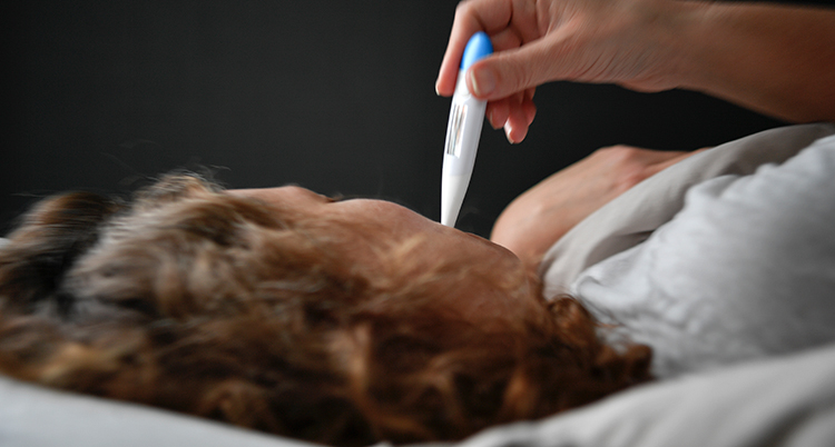 En kvinna har en termometer i munnen för att se om hon har feber.