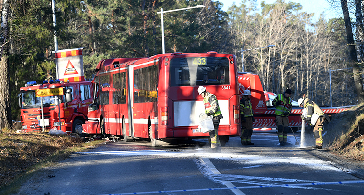 En röd buss står på vägen. Personal från räddningstjänst står på vägen.