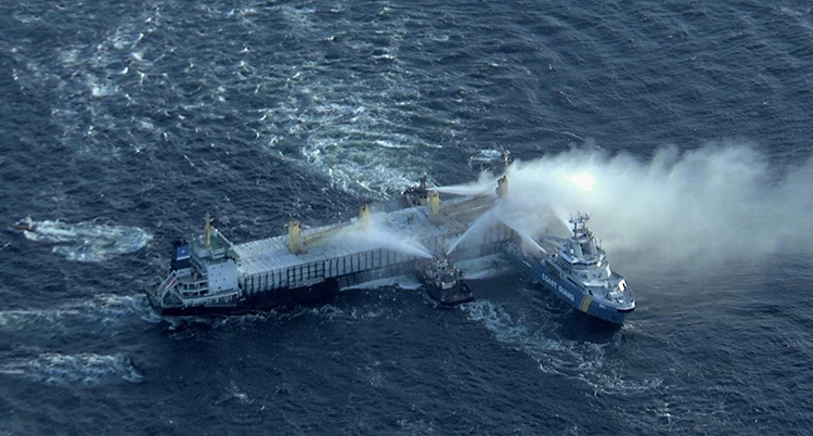 En bild som är tagen från luften. Bilden visar ett fartyg ute på havet. Några mindre båtar ligger bredvid och sprutar vatten på fartyget.