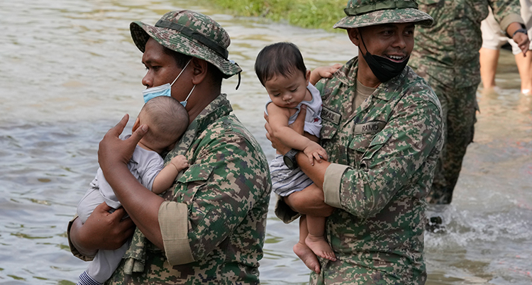 Två män i militärkläder bär varsitt spädbarn i midjehögt vatten.