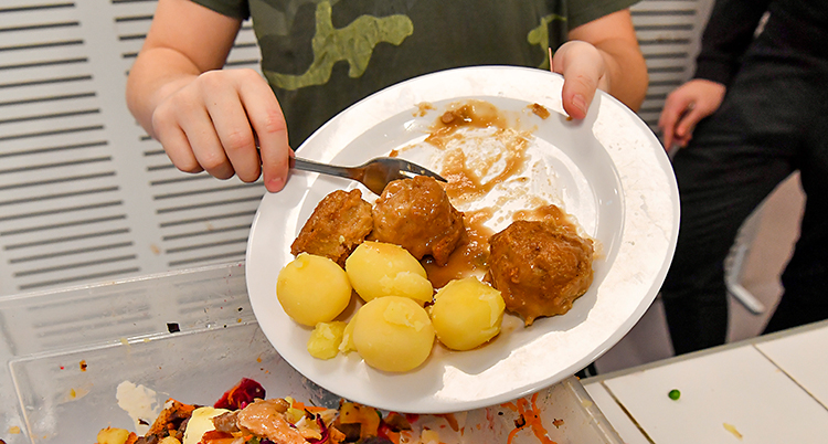 En person slänger potatis och kött från en tallrik.