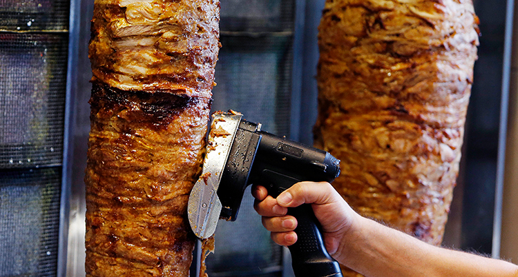 En person skär loss kött från ett stort spett med kebab.