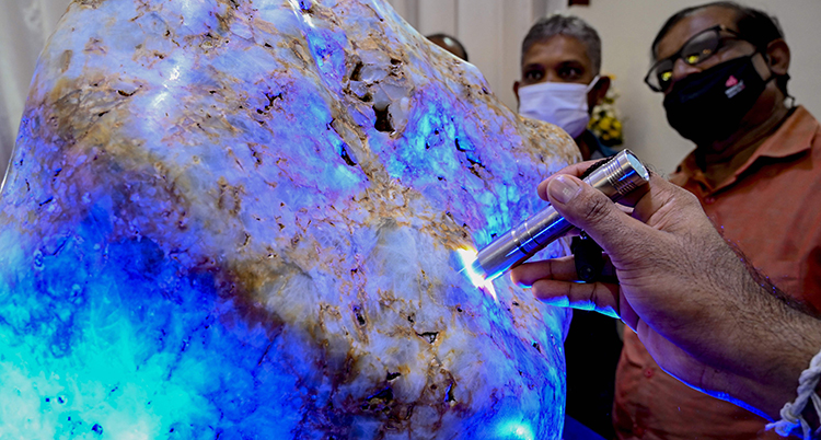 En hand lyser med en ficklampa på en stor vitblå sten. Två personer syns bakom.