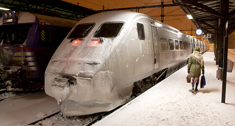 En ensam person på en snöig perrong går mot ett grått tåg