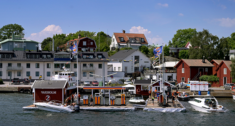Båtar kör in vid en sjömack, en stad syns i bakgrunden.