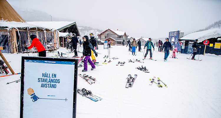 Det är snö på marken. Människor går runt och bär på skidor och det ligger skidor på marken.