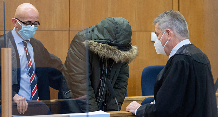 Den anklagade mannen i rätten. Han står med nerböjt huvud. Kapuschongen från hans vinterjacka döljer hans ansikte.