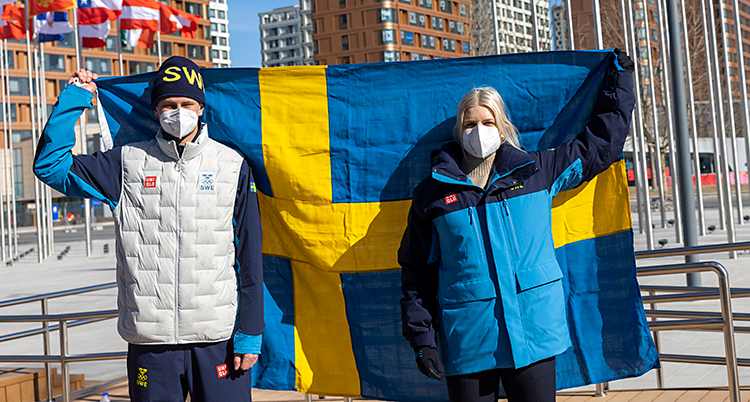 De står bredvid varandra och håller tillsammans upp en svensk flagga bakom ryggarna. De har munskydd på sig.