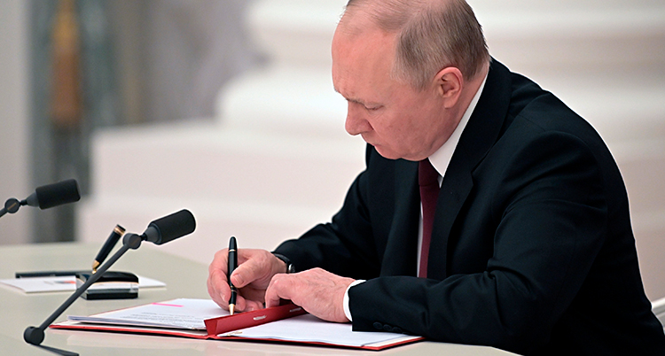 Vladimir Putin sitter vid ett skrivbord och skriver på ett papper.