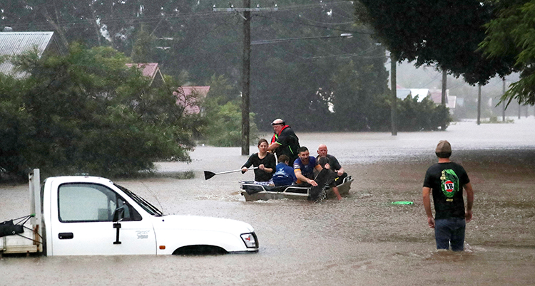 Det är översvämning på en gata. Vattnet står högt upp över en bil. Människor går i högt vatten.