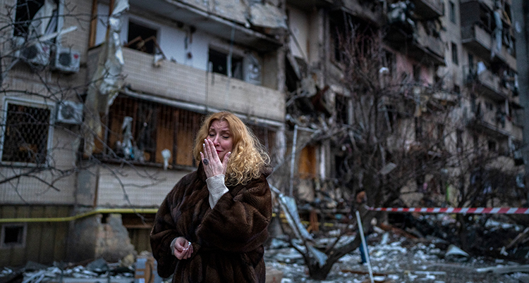 En kvinna gråter framför ett förstört hus.