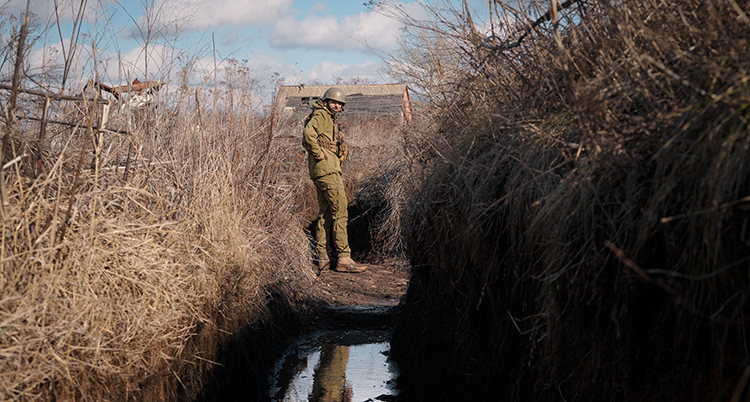 En soldat står i ett dike och tittar mot kameran.