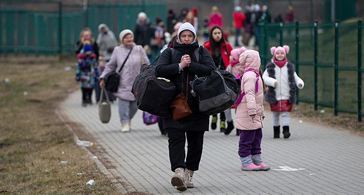 Kvinnor och barn går på en väg med sina väskor.