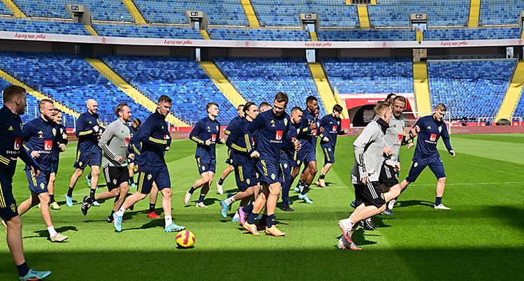 Bilden är tagen på en stadion för fotboll. De svenska spelarna springer på gräset.